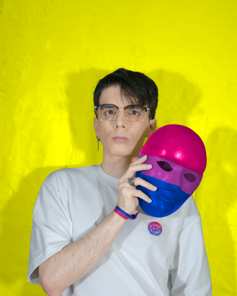 Alex Robles quitándose una máscara con la bandera de la bisexualidad
